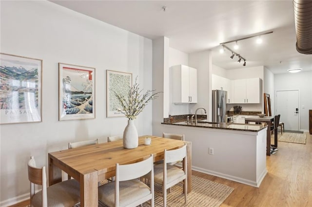 dining area featuring track lighting, baseboards, and light wood-style floors