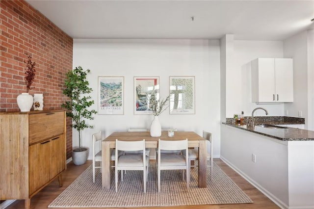 dining space featuring brick wall, baseboards, and wood finished floors