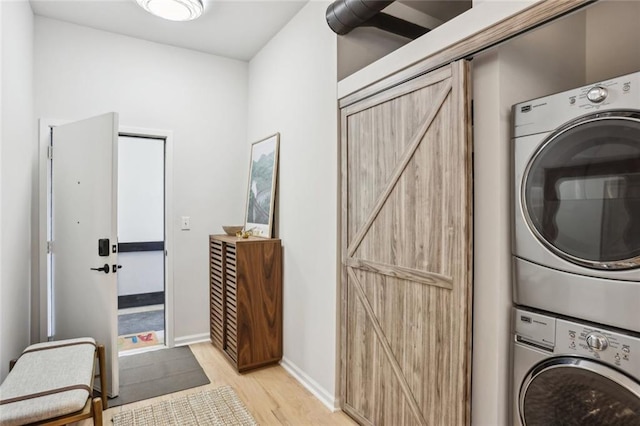 laundry area featuring stacked washing maching and dryer, a barn door, light wood-style floors, baseboards, and laundry area