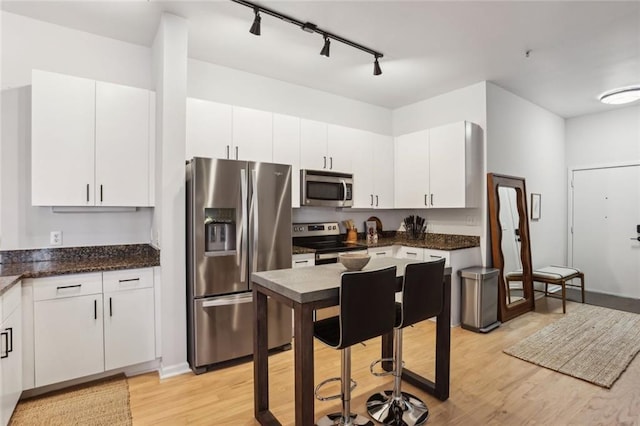 kitchen with dark stone counters, light wood-style flooring, white cabinets, and stainless steel appliances