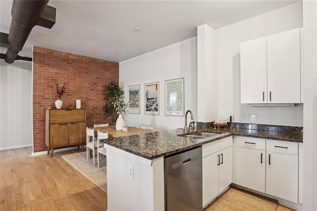 kitchen with dishwasher, dark stone counters, a peninsula, white cabinets, and a sink