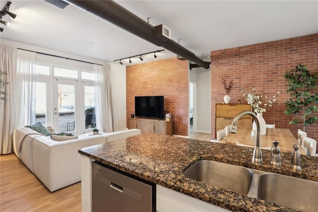 kitchen with a sink, stainless steel dishwasher, open floor plan, light wood-style floors, and brick wall