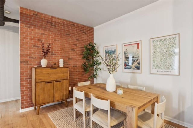 dining room with light wood-style flooring, brick wall, and baseboards