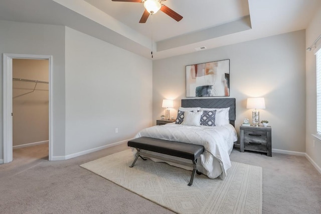 carpeted bedroom with a closet, a walk in closet, ceiling fan, and a tray ceiling