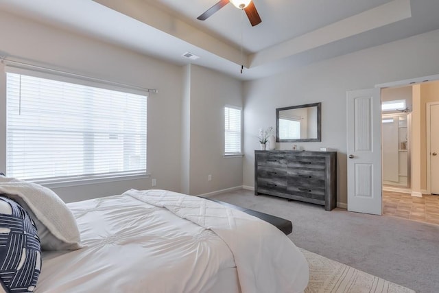 bedroom featuring light carpet, multiple windows, a raised ceiling, and ceiling fan