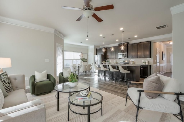 living room featuring sink, crown molding, ceiling fan, and light wood-type flooring