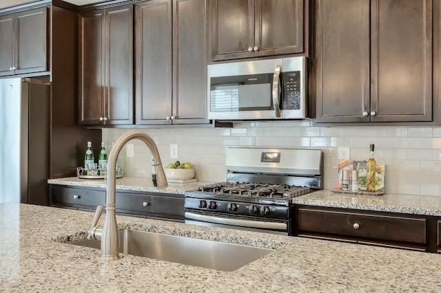 kitchen featuring dark brown cabinetry, sink, stainless steel appliances, and light stone countertops