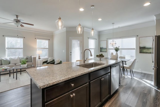 kitchen with appliances with stainless steel finishes, pendant lighting, sink, light stone countertops, and a center island with sink