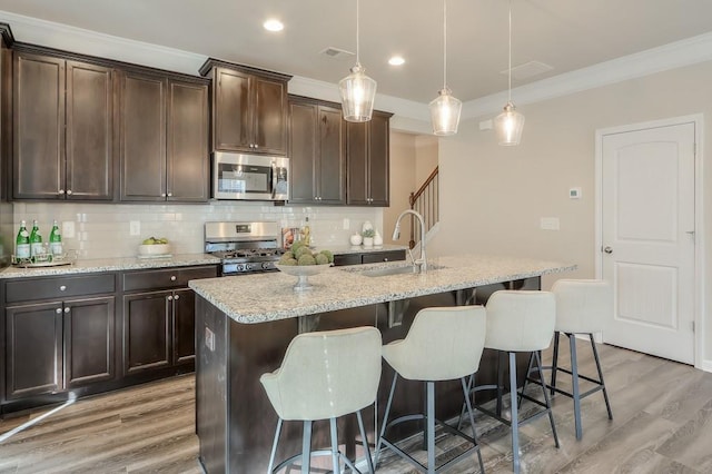 kitchen featuring sink, dark brown cabinets, pendant lighting, stainless steel appliances, and a kitchen island with sink