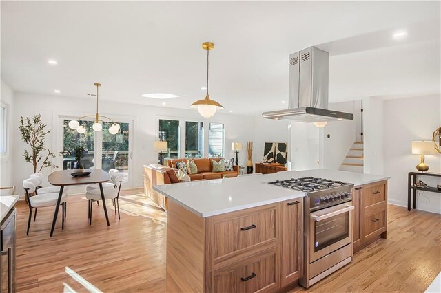 kitchen with wall chimney range hood, appliances with stainless steel finishes, a sink, brown cabinetry, and visible vents