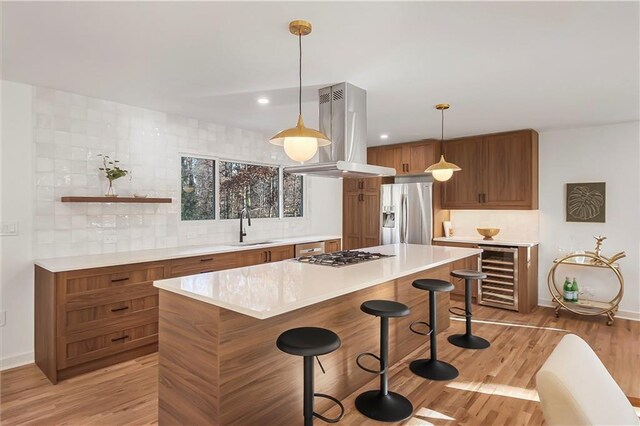 kitchen featuring brown cabinetry, a kitchen bar, island range hood, appliances with stainless steel finishes, and beverage cooler