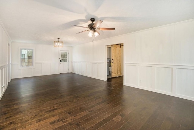 empty room with crown molding, dark wood-style flooring, a decorative wall, and ceiling fan with notable chandelier