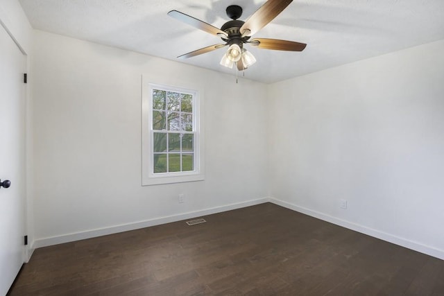 spare room with baseboards, a ceiling fan, visible vents, and dark wood-style floors