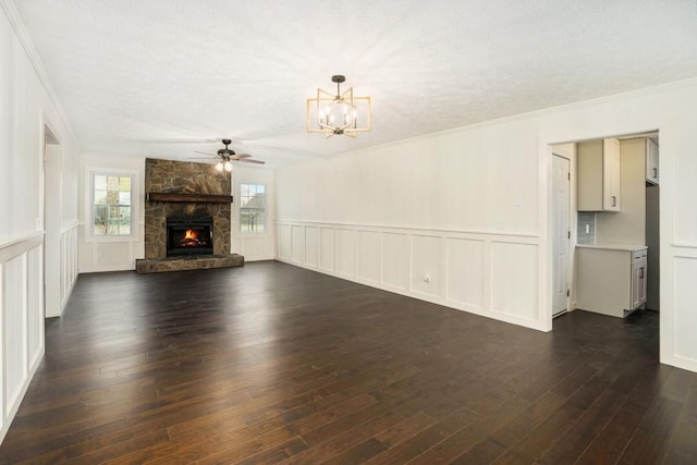 unfurnished living room with ceiling fan with notable chandelier, a stone fireplace, plenty of natural light, and dark wood finished floors