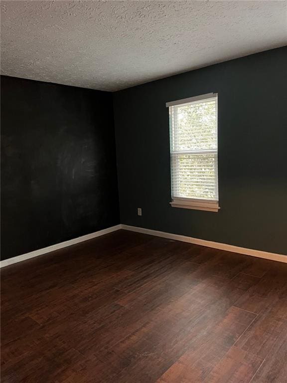 unfurnished room featuring dark wood-style floors, a textured ceiling, and baseboards