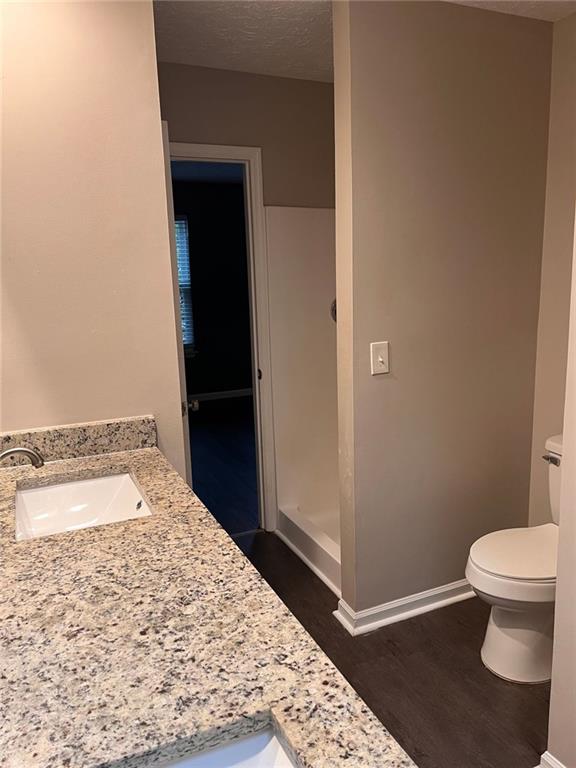 bathroom featuring baseboards, toilet, vanity, wood finished floors, and a textured ceiling