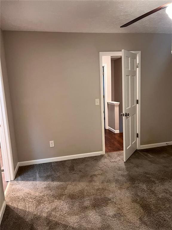 unfurnished room with a textured ceiling, baseboards, and dark colored carpet