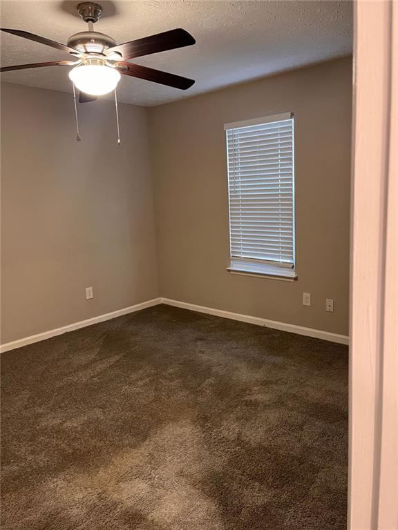 empty room featuring dark colored carpet, baseboards, a textured ceiling, and ceiling fan