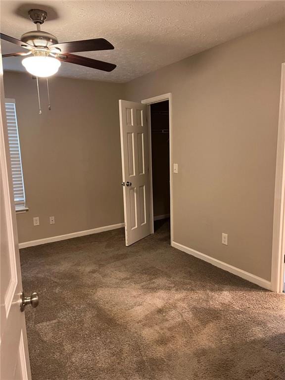 empty room featuring ceiling fan, baseboards, dark colored carpet, and a textured ceiling