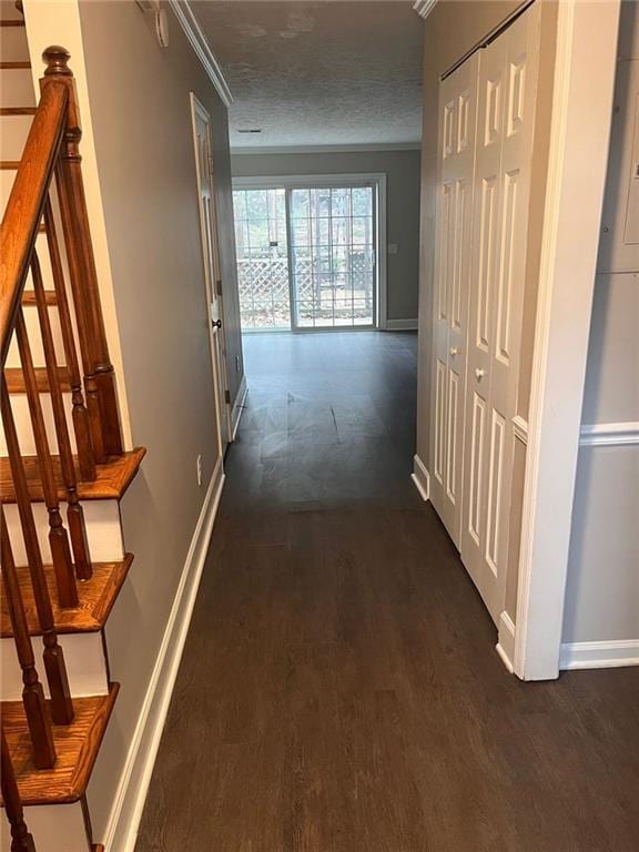 hall featuring a textured ceiling, dark wood-type flooring, baseboards, and ornamental molding