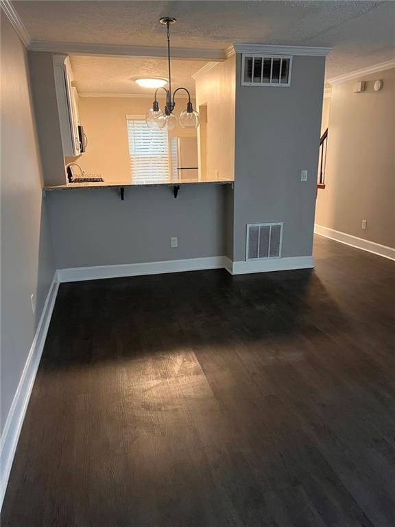 empty room with dark hardwood / wood-style flooring, a textured ceiling, ornamental molding, and a chandelier