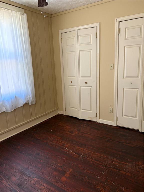 unfurnished bedroom featuring dark wood finished floors, baseboards, a closet, and a textured ceiling