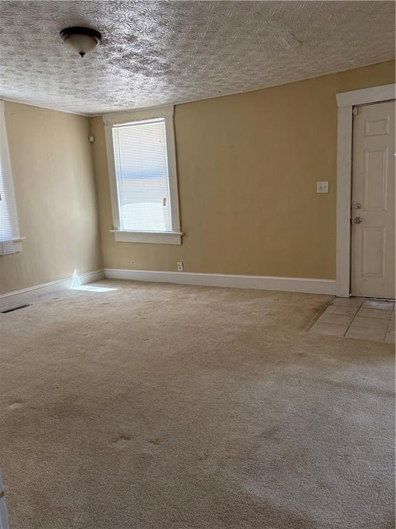 empty room featuring a textured ceiling, baseboards, and light carpet