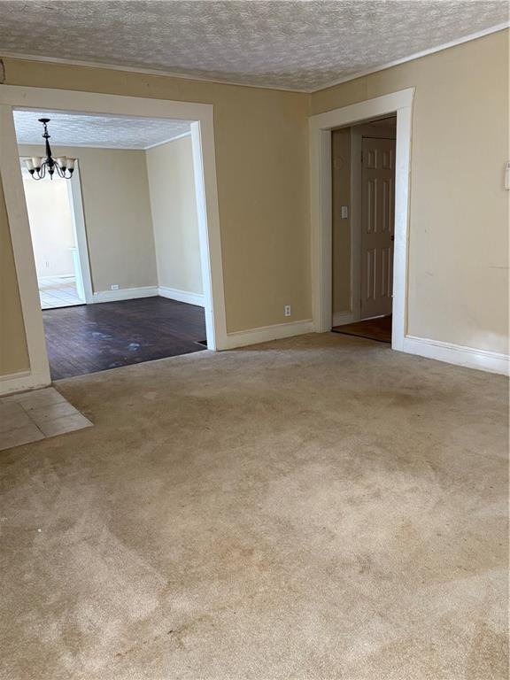 unfurnished room featuring baseboards, a textured ceiling, an inviting chandelier, and carpet floors