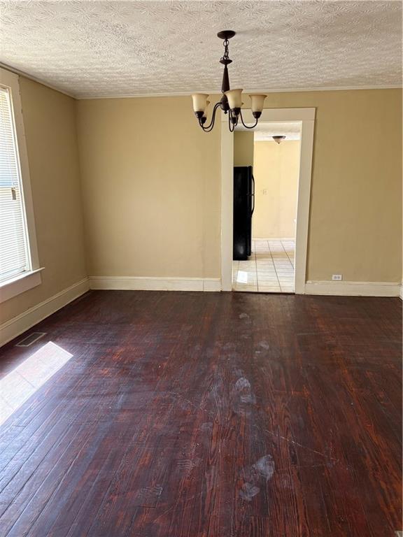 spare room with baseboards, wood-type flooring, a textured ceiling, and a chandelier