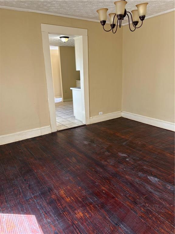 spare room featuring baseboards, a chandelier, ornamental molding, hardwood / wood-style flooring, and a textured ceiling