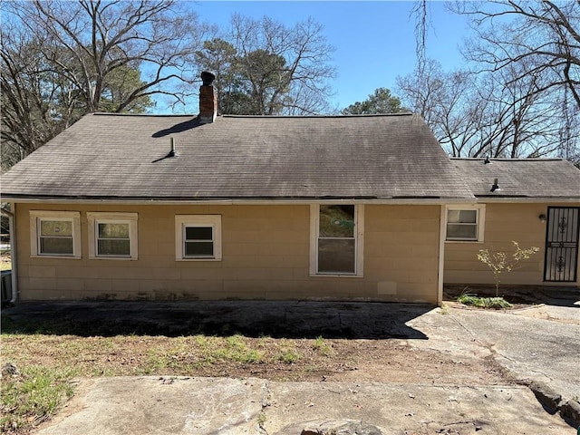 rear view of property featuring a chimney and roof with shingles