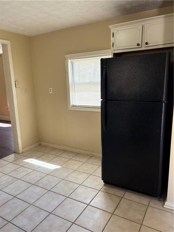kitchen featuring a textured ceiling, white cabinetry, freestanding refrigerator, light tile patterned flooring, and baseboards