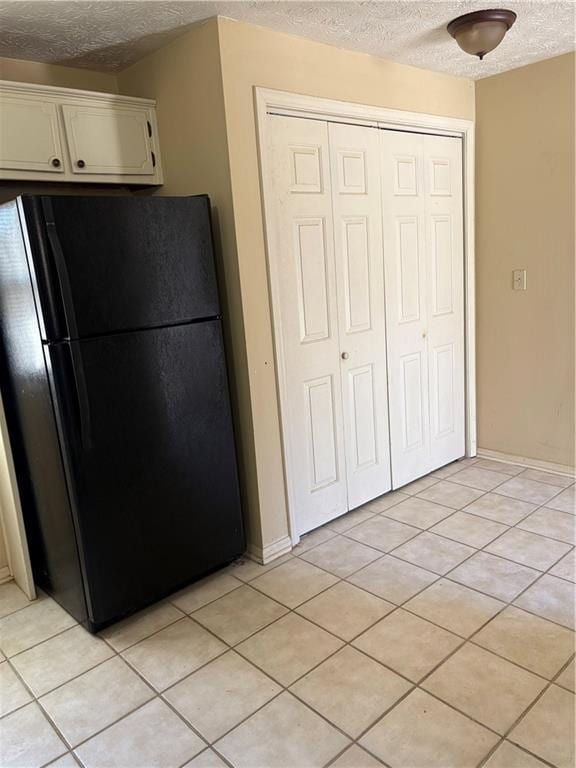 kitchen featuring light tile patterned floors, white cabinetry, a textured ceiling, and freestanding refrigerator