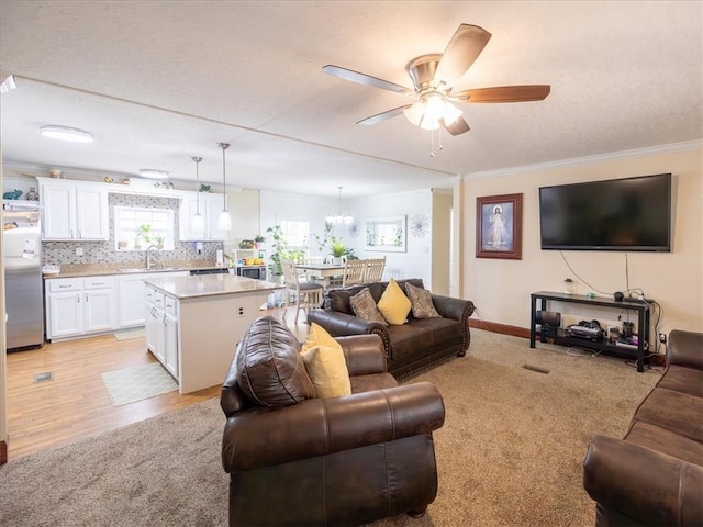 living area featuring crown molding, light wood-style floors, light carpet, ceiling fan, and baseboards