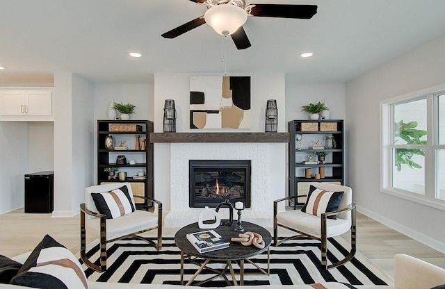 sitting room featuring ceiling fan, light wood-type flooring, and a brick fireplace