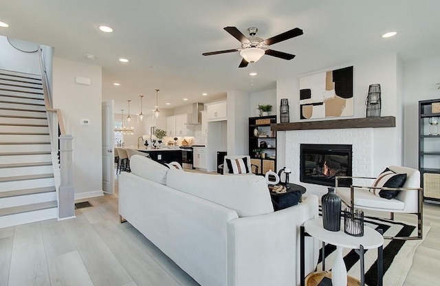 living room with light wood-type flooring, ceiling fan, and a fireplace