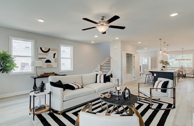 living room with ceiling fan with notable chandelier and light wood-type flooring