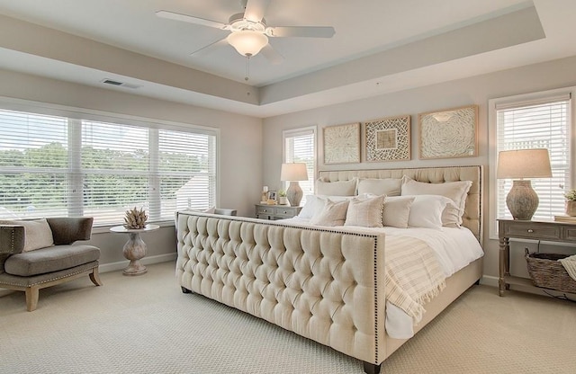 carpeted bedroom featuring ceiling fan, multiple windows, and a raised ceiling