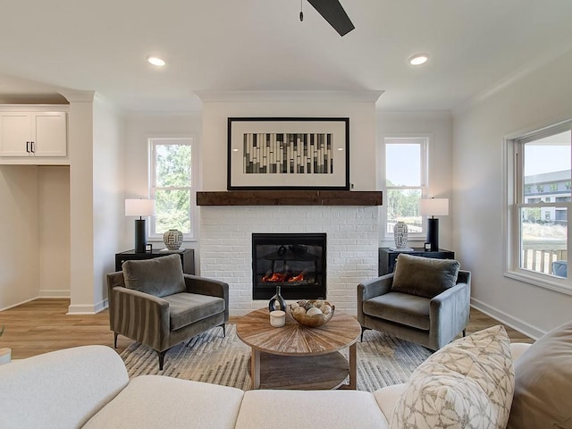 living room with ceiling fan, light hardwood / wood-style flooring, a brick fireplace, and ornamental molding