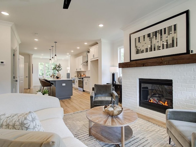 living room with light hardwood / wood-style flooring, a brick fireplace, and crown molding