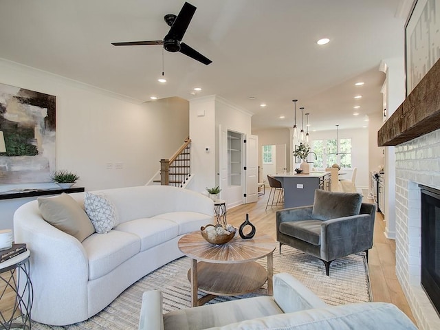 living room featuring ceiling fan, light wood-type flooring, a brick fireplace, and crown molding