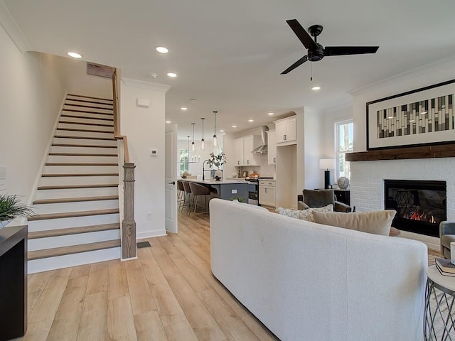 living room with crown molding, a brick fireplace, light hardwood / wood-style flooring, and ceiling fan