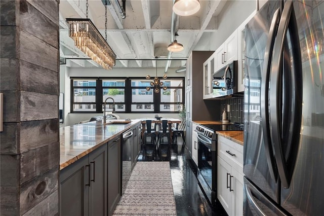 kitchen featuring appliances with stainless steel finishes, a sink, white cabinetry, light stone counters, and a chandelier