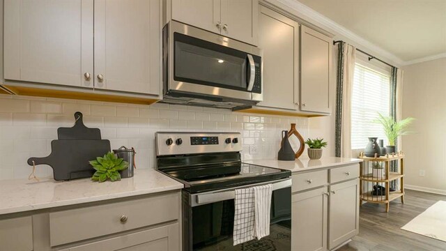 kitchen featuring appliances with stainless steel finishes, backsplash, light stone counters, crown molding, and light hardwood / wood-style flooring