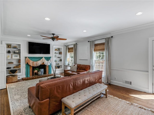 living room with a brick fireplace, visible vents, ornamental molding, and hardwood / wood-style flooring