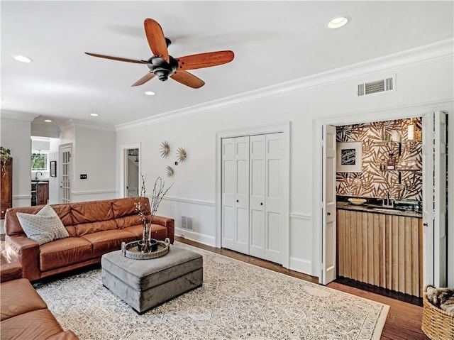 living room featuring visible vents, a ceiling fan, crown molding, and wood finished floors