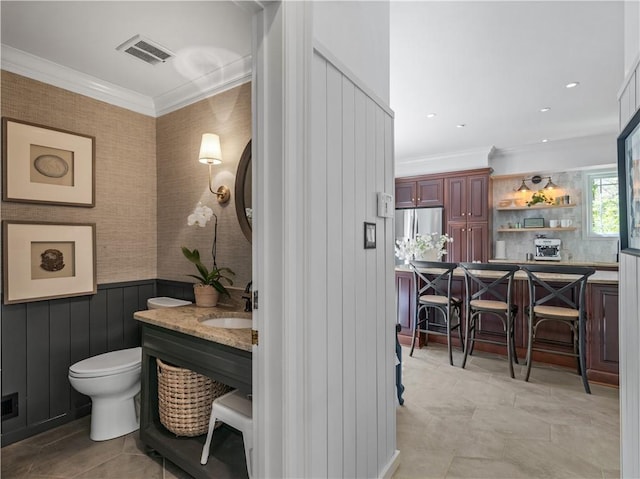 bathroom featuring visible vents, ornamental molding, vanity, toilet, and a wainscoted wall