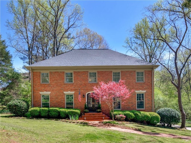 colonial-style house featuring brick siding, a shingled roof, and a front yard