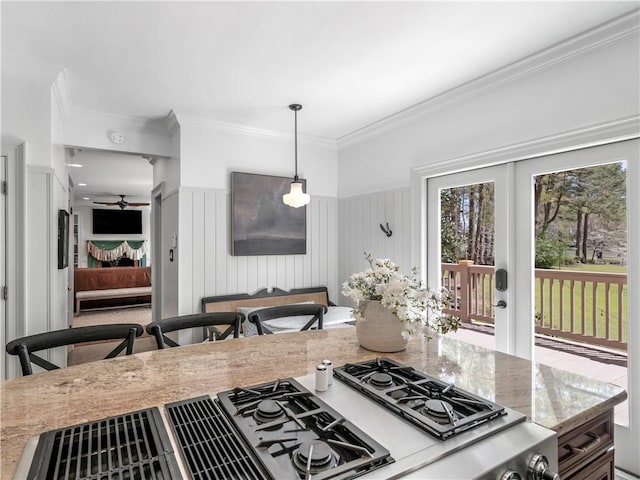 kitchen featuring ceiling fan, hanging light fixtures, wainscoting, light stone counters, and ornamental molding