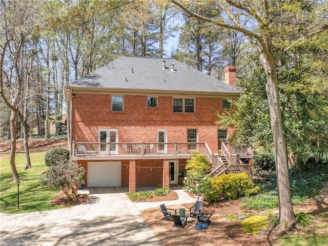 back of house featuring a garage, a deck, a chimney, stairs, and concrete driveway